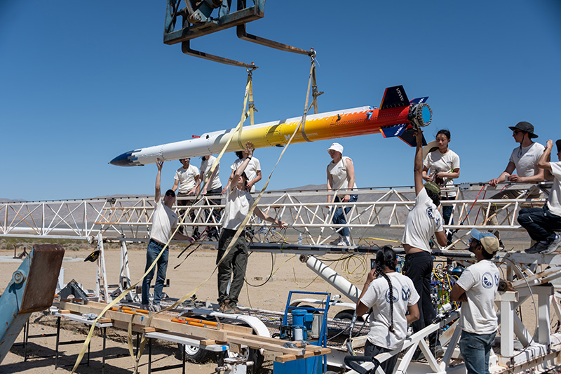 Members of the MASA rocket team loading their rocket onto the launch trail before raising the rail vertically.