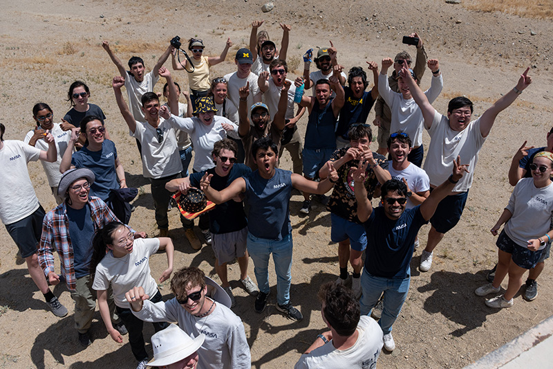A group of the MASA rocket team standing in the desert with their hands in the air cheering.