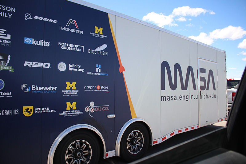 The MASA team trailer being pulled down the road with all of their sponsors listed on the side.
